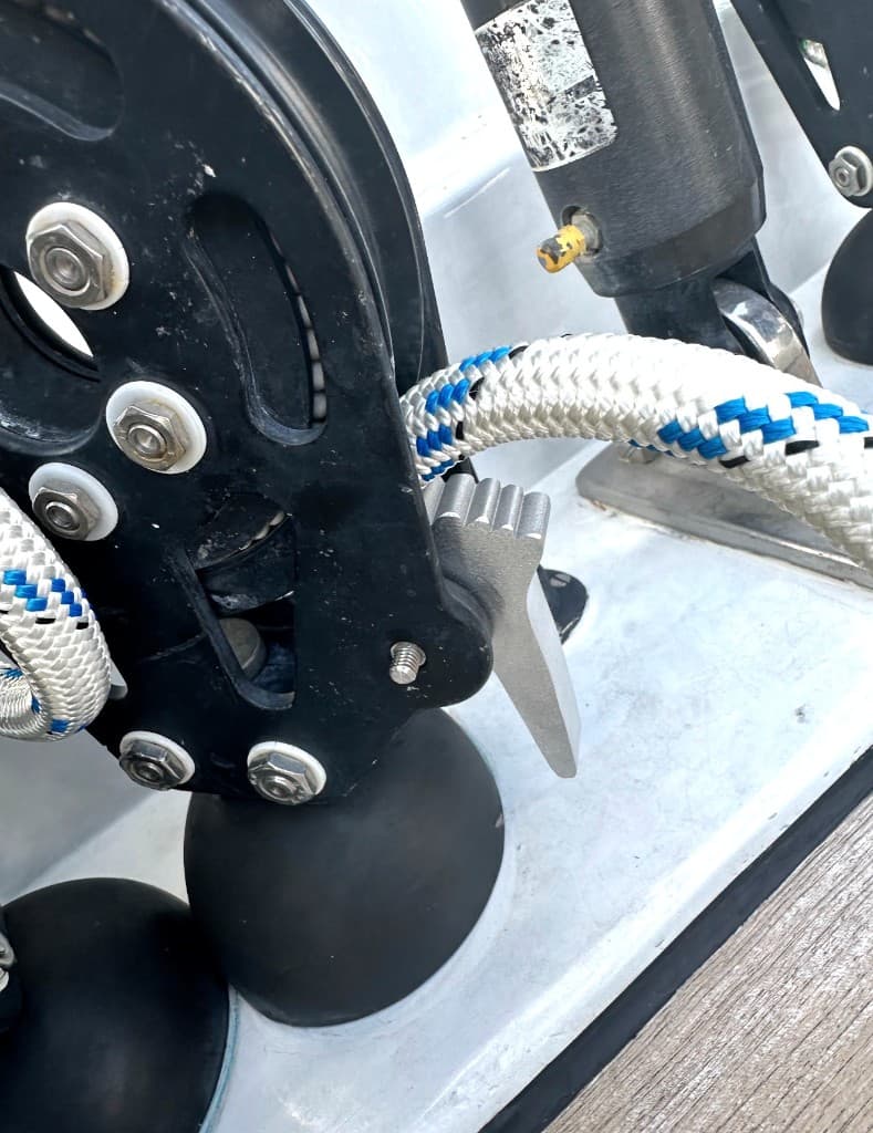 Braided line running through a black deck block and metal cam cleat on a white and teak deck