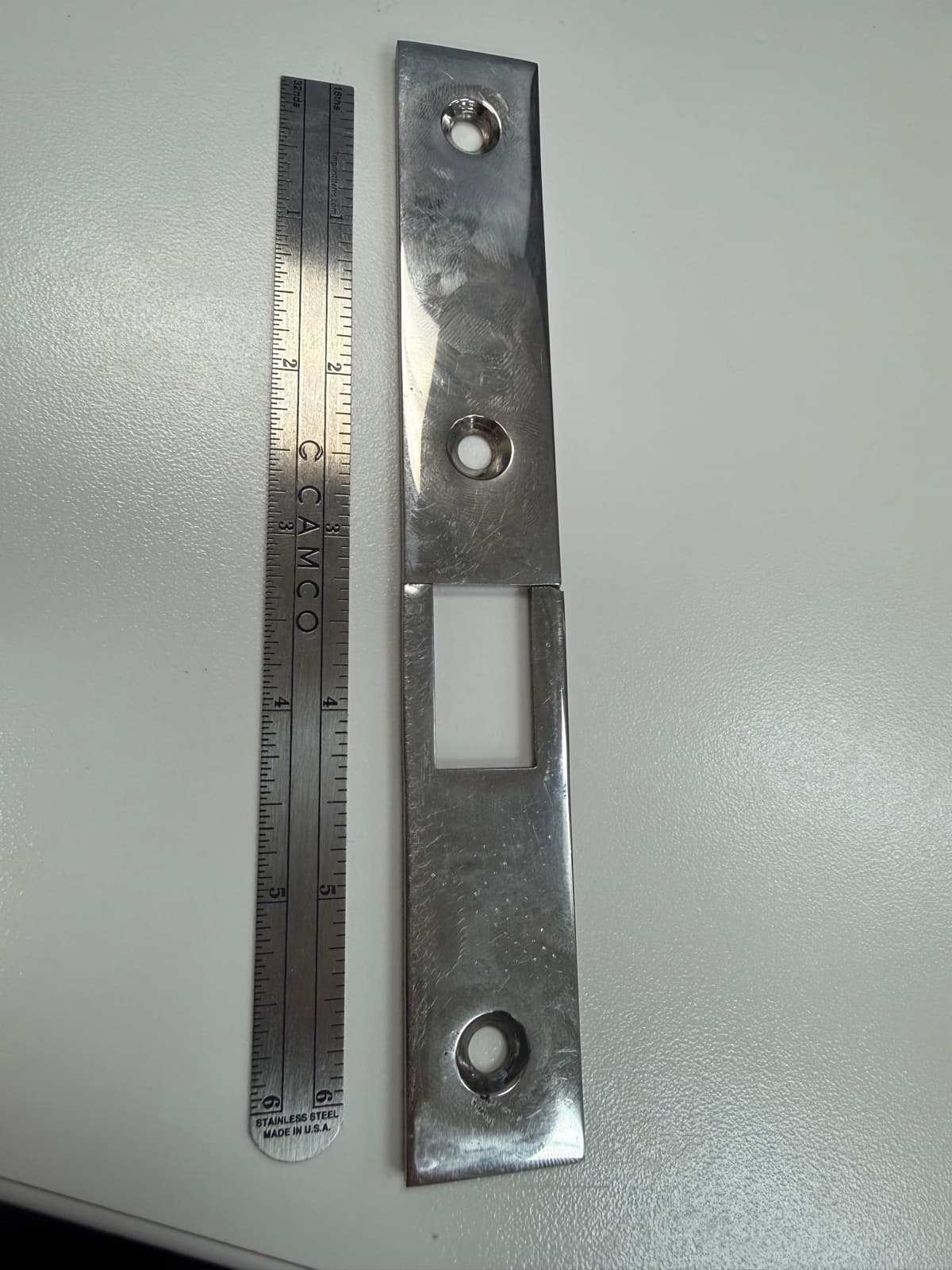 Original broken latch bracket photographed next to a ruler for scale