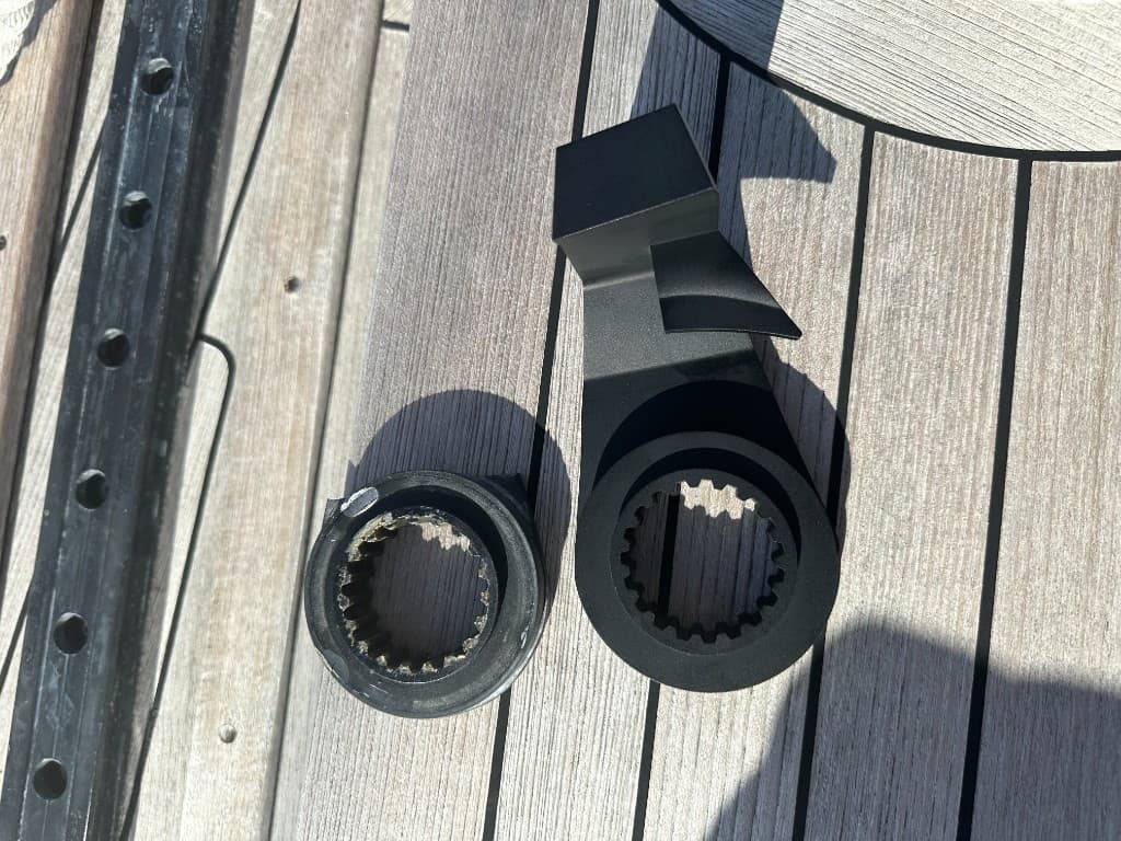 Fractured black metal hub beside a complete black replacement windlass rope stop on a wooden deck