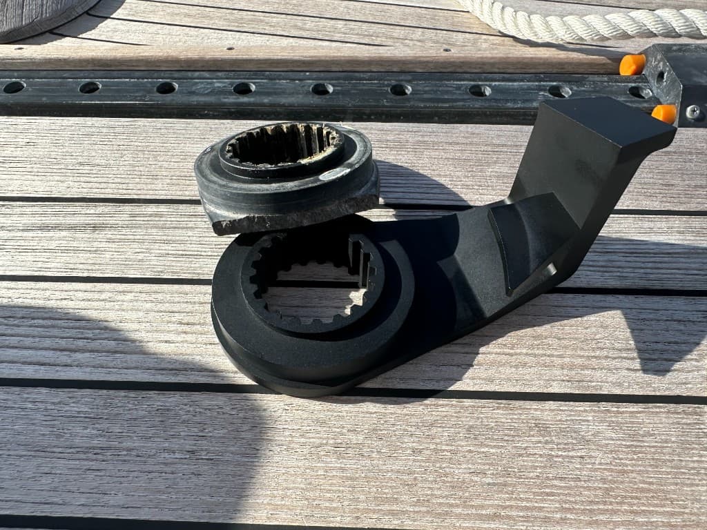 Broken original windlass rope stop resting on a new black replacement arm on teak decking